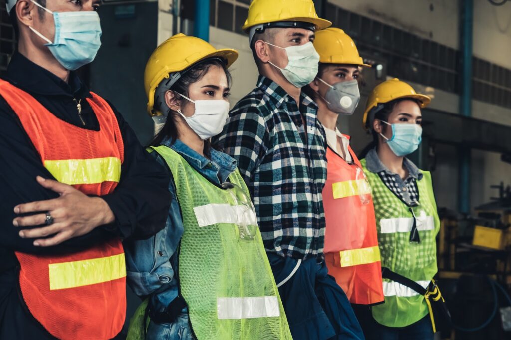 a group of workers standing together while wearing face masks and hard hats