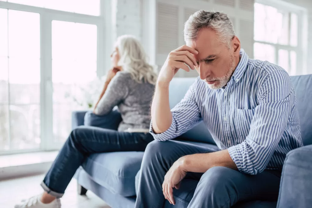 a senior couple sitting on opposite ends of a couch after speaking about divorce